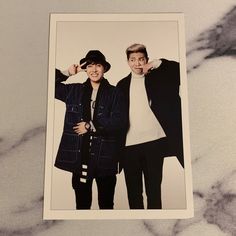 two young men standing next to each other in front of a marble background with one holding his hat