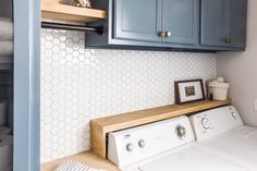 a washer and dryer in a small room with blue cabinetry, white hexagonal tiles on the backsplash