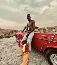 a man sitting on the hood of a red car with flowers in his booties