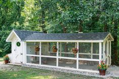 a white chicken coop sitting in the middle of a yard with potted plants on it