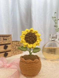 a crocheted sunflower sitting in a pot next to a bottle of perfume