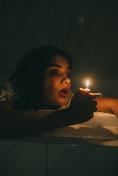 a woman holding a lit candle in her hand and looking at the camera while laying down