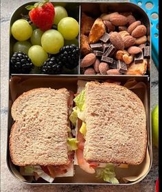 a lunch box with two sandwiches, fruit, nuts and chocolates on the side