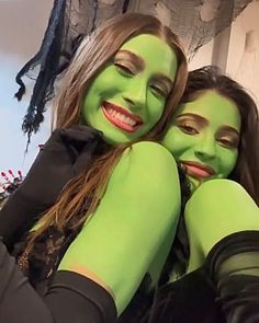 two women in green make up their faces and smile at the camera while posing for a photo