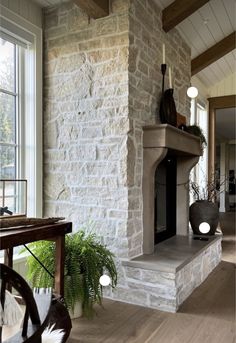 a living room with a stone fireplace next to a large window and potted plant