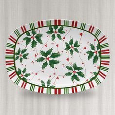 a white and green platter with holly leaves on it's rim is hanging from the wall