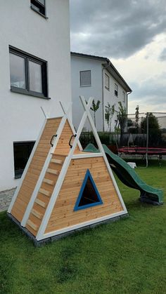 a house made out of wood with a slide in the grass next to it and two children's play areas