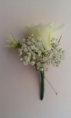 a white rose and baby's breath boutonniere on a pink wall