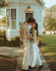 a young man and woman are kissing in front of a white house on the sidewalk