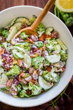 a white bowl filled with broccoli salad next to grapes and lemon wedges