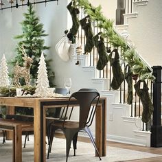 a dining room table with christmas decorations hanging from the banister and stockings on the wall