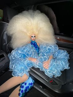 a doll sitting in the back seat of a car wearing a blue dress and wig