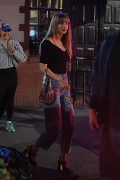 a woman in black shirt and jeans walking down street with handbag on her hip