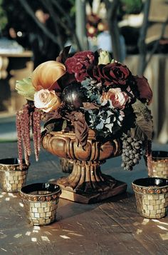 a vase filled with lots of flowers sitting on top of a table next to cups