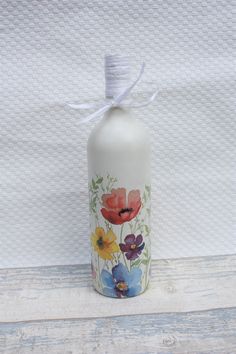 a bottle with flowers painted on it sitting on a wooden table next to a white wall