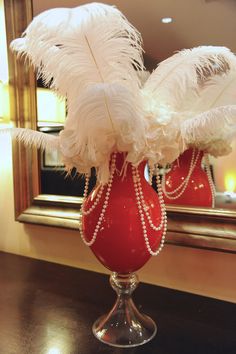 there is a red vase with white feathers in it on the table next to a mirror