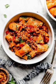 two bowls filled with pasta and sauce on top of a table next to silverware