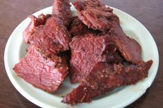 a white plate topped with sliced beef on top of a wooden table next to a cup