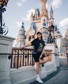 a woman posing for a photo in front of the castle at disney world with her arms out