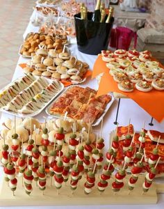 a table topped with lots of food on top of a white table covered in orange cloths