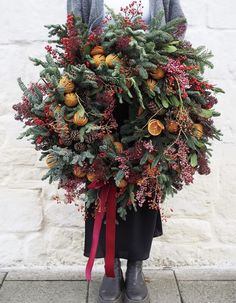 a wreath with oranges and berries tied to it on a pole in front of a white brick wall