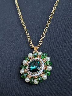 Make a statement on all occasions with this gorgeous, one-of-a-kind hand beaded pendant.  This piece features an emerald colored Swarovski Rivoli encased in delicate beadwork and strung on a brass 18k gold-plated chain. Beaded Emerald Jewelry Gift, Green Beaded Necklaces With Large Pendant For Gift, Green Beaded Necklace With Large Pendant For Gift, Beaded Emerald Jewelry For May Birthstone, Elegant Beaded Emerald Necklaces, Elegant Beaded Emerald Necklace, Green Crystal Beaded Necklaces As Gift, Green Crystal Beaded Necklace For Gift, Emerald Faceted Beads Necklace As Gift