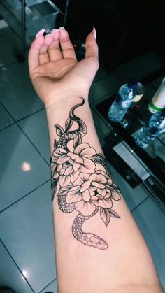 a woman's arm with a snake and flowers tattoo on it