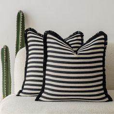 two black and white striped pillows sitting on top of a couch next to a cactus