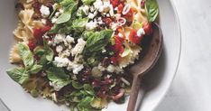 a white bowl filled with pasta salad and spinach on top of a marble table