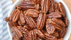 a white bowl filled with pecans sitting on top of a wooden table next to a blue and white towel