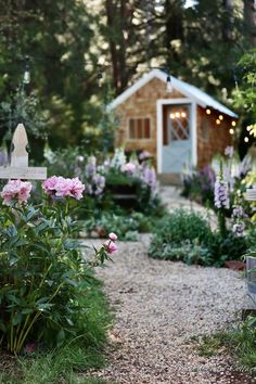 a garden with lots of flowers next to a small house in the background and lights on