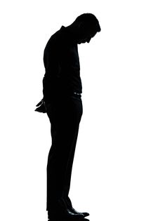 the silhouette of a man in a suit and tie is looking down at his cell phone