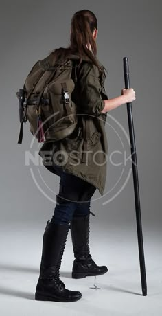 a woman in black boots is holding a cane and looking at the ground with her back to the camera