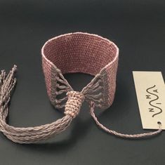 a crocheted bracelet with tassels is shown next to a tag on a black surface