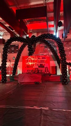 an indoor stage set up for a party with balloons and lights on the ceiling, surrounded by red lighting