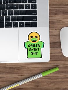 a green shirt guy sticker sitting on top of a desk next to a laptop