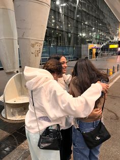 two women hugging each other in front of a large building at an airport with lights on