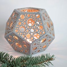 a decorative candle holder with holes in the center on a pine tree branch, against a white background