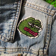 a close up of a person's jean jacket with a green frog embroidered on it