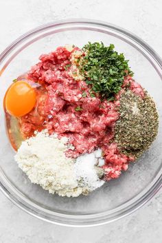 ingredients for meatballs in a glass bowl on a marble counter top, including eggs and seasoning