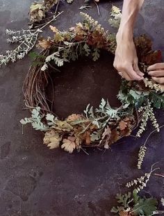 someone is making a wreath out of branches and leaves on the ground with their hands