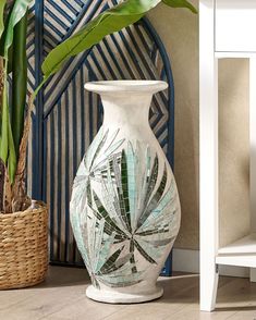 a white vase sitting on top of a wooden floor next to a potted plant