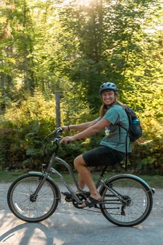 a woman riding a bike down a street next to some bushes and trees in the background