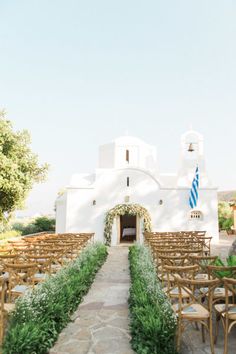 an outdoor wedding venue with rows of wooden chairs and greenery on the side of the aisle