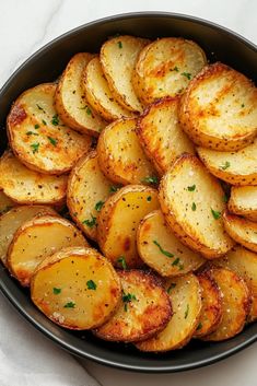 cooked potatoes with parsley in a black bowl on a white tablecloth, top view