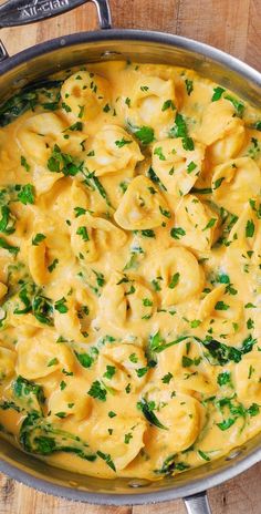 a pan filled with pasta and spinach on top of a wooden table