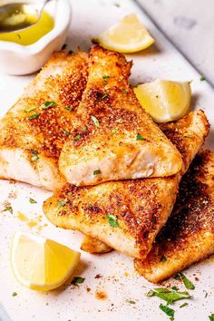 three pieces of chicken on a white plate with lemons and seasoning next to it