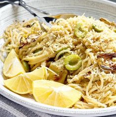 a white bowl filled with pasta and lemon wedges on top of a gray table cloth