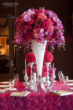 a tall white vase filled with lots of purple and red flowers on top of a table