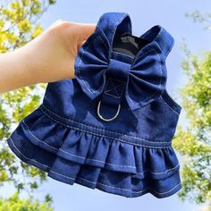 a hand holding up a blue jean dress with a bow on the front and bottom